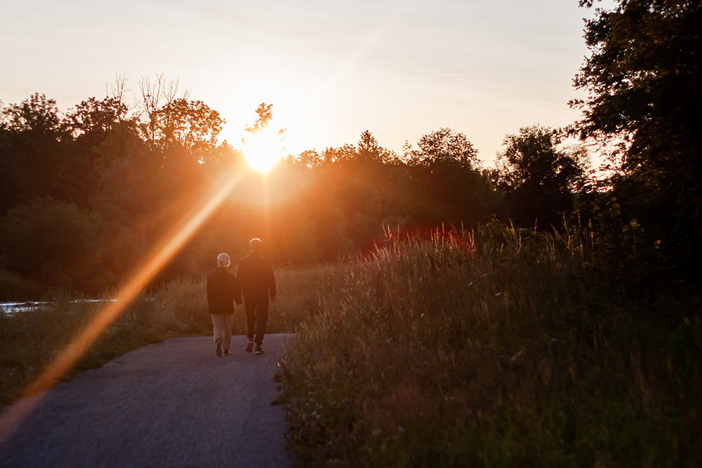 two persons walking in a wooded area in the sunset